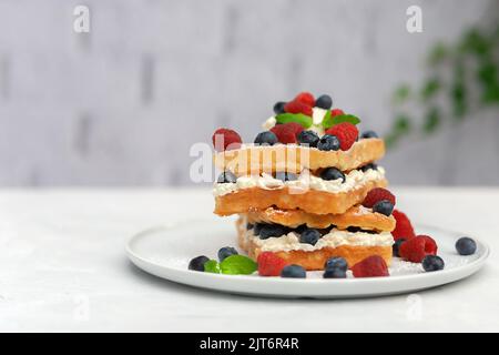 Fresh Viennese or Belgian waffles on a plate with fresh raspberries and blueberries and whipped cream. Stock Photo