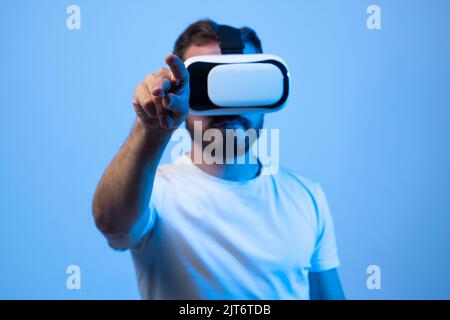 Mature bearded man interacting with the metaverse while wearing virtual reality goggles. Young man using his finger to press a virtual button. Stock Photo