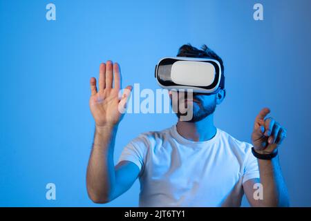 Young bearded man in VR helmet playing VR games on colourful background. VR gaming. Stock Photo