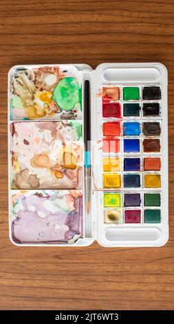 Top view of colorful watercolor palette and brush close-up on the wooden table, back to the school, selective focus, noise effect Stock Photo