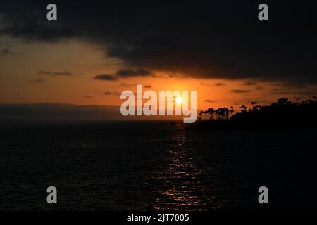 A bright orange sky as the sun sets between layers of clouds over Twin Points, Laguna Beach, California. Stock Photo