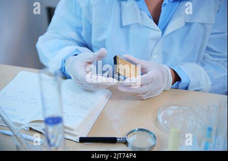 Close-up . Scientist chemist hands in medical gloves holding a container with litmus paper for measuring the PH Stock Photo
