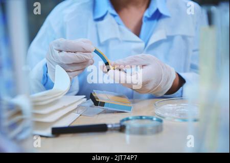 Cropped view of a scientist holding PH indicator strip, litmus or reagent paper for measuring alkalinity and acidity. Stock Photo