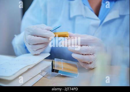 Lab technician hands in medical gloves holding a container with litmus paper for measuring the PH, alkalinity, acidity Stock Photo