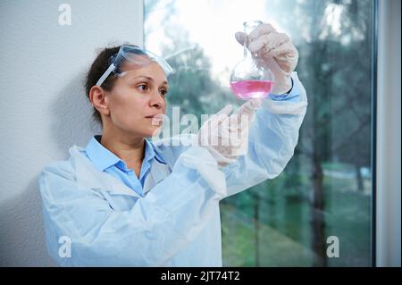 Pretty woman scientist pharmacologist works on new generation drug or vaccine, holds flask, conducts science experiment Stock Photo