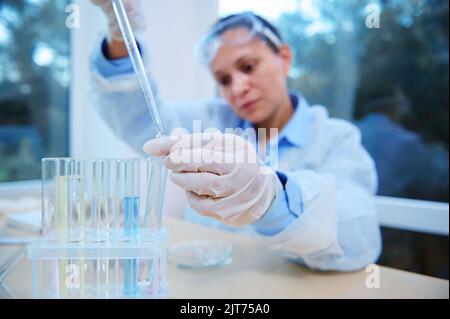 Chemist scientist laboratory asistant using a graduated pipette, dripping reagent into test tubes, making analizes Stock Photo