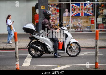 LONDON - May 20, 2022: Man in helmet on white motor scooter stopped on road Stock Photo