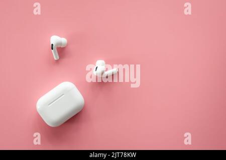 Wireless in-ear headphones with a case on a pink background, flat lay. Stock Photo