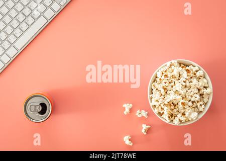 A bowl of popcorn, a keyboard and a can of drink on a pink background. Stock Photo