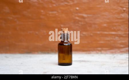 Small brown medicine bottle on white stone table and blurry orange painted background. Stock Photo