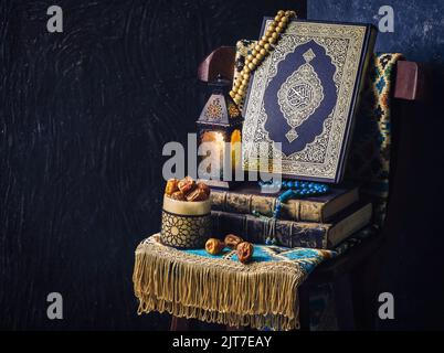 Islamic Holy Book 'Quran' placed with rosary beads, oriental Ramadan lantern, fresh dates and prayer rug on wooden chair. Stock Photo