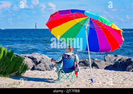 A woman sits beneath a beach umbrella on Dauphin Island East End Beach, Aug. 27, 2022, in Dauphin Island, Alabama. Stock Photo