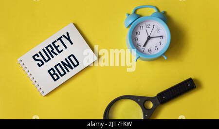 On a yellow background, an alarm clock, notepads, a magnifying glass and a notepad with the inscription SURETY BOND. business concept Stock Photo