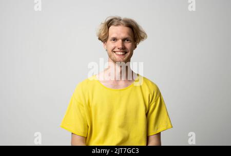 Young smiling man in a yellow t-shirt over gray background. Stock Photo