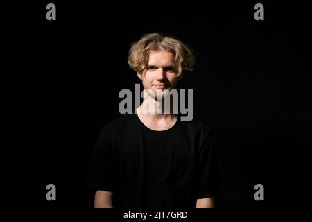 Young smiling man in a black t-shirt over black background. Stock Photo