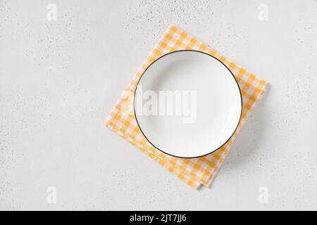 White empty plate with yellow checkered towel on white background. Stock Photo