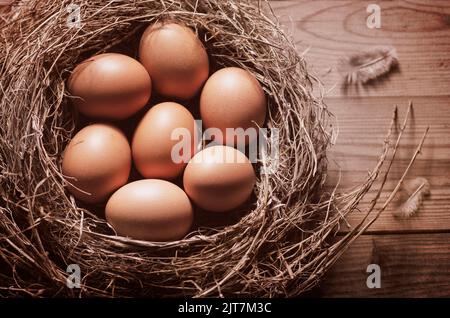 Still life with close-up view of raw chicken eggs in nest on rustic wooden background. Stock Photo