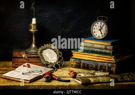 Classic still life with vintage books placed with old clock, glasses, candlestick, pipe and empty broken frame on rustic wooden background. Stock Photo