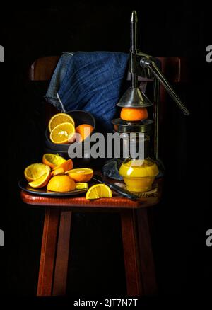 Orange juice bottle placed with old traditional squeezer and fresh oranges on wooden chair. Stock Photo