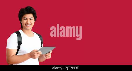 Happy young Asian man holding tablet computer on red background with space for text Stock Photo
