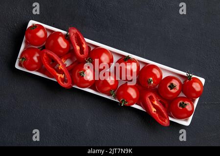 Fresh raw cherry tomatoes and paprika slices on a white rectangular dish on a black concrete table Stock Photo
