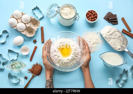 Female hands with ingredients for preparing cookies and cutters on color background Stock Photo