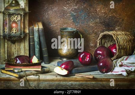 Classic still life with fresh red apples placed with antique jar and old books on rustic wooden background. Stock Photo