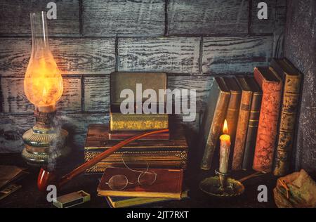 Classic still life with illuminated candle placed with old lamp, books and antique pipe on rustic background. Stock Photo