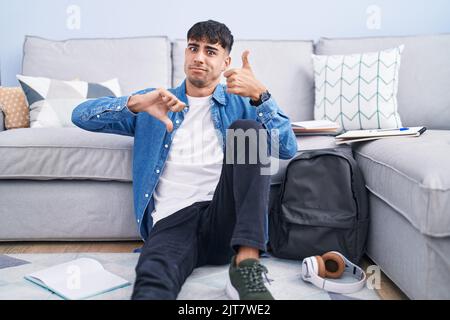 Young hispanic man sitting on the floor studying for university doing thumbs up and down, disagreement and agreement expression. crazy conflict Stock Photo