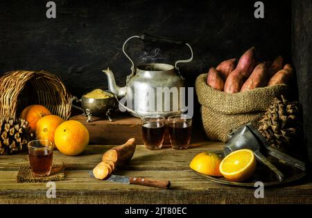 Classic still life with fresh oranges placed with bag of sweet potatoes and hot tea on rustic wooden background. Stock Photo