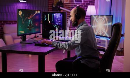 Gamer playing fast paced space shooter simulation screaming victorious at the computer screen after winning difficult level. Caucasian man celebrating victory in internet multiplayer action game. Stock Photo