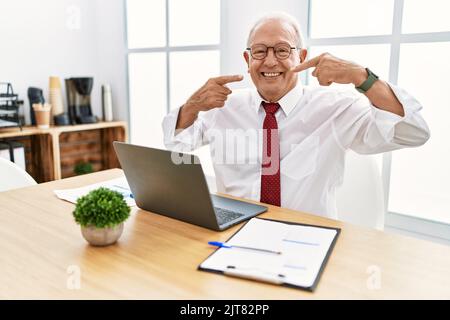 Senior man working at the office using computer laptop smiling cheerful showing and pointing with fingers teeth and mouth. dental health concept. Stock Photo