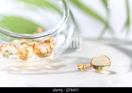 Serum capsules for healthy skin. Blurred background, glass jar with the capsules and green palm leaf. Stock Photo