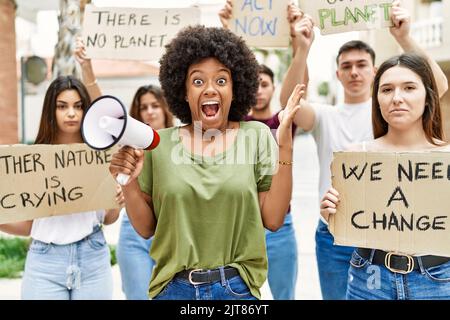 Group of young friends protesting and giving slogans at the street celebrating victory with happy smile and winner expression with raised hands Stock Photo