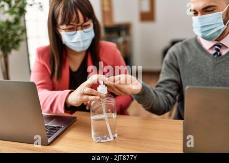 Two hispanic business workers wearing medical mask using sanitizer hands gel at the office. Stock Photo