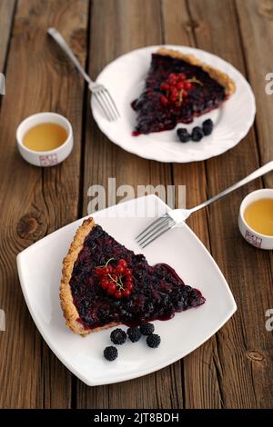 Two pieces of tart with black currant and blackberry filling and green tea on wood background Stock Photo