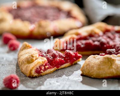 Slice of perfect raspberry galette. Delicious rustic homemade tart with frozen or fresh raspberries on gray background. Beautiful piece of galette with raspberries, copy space Stock Photo