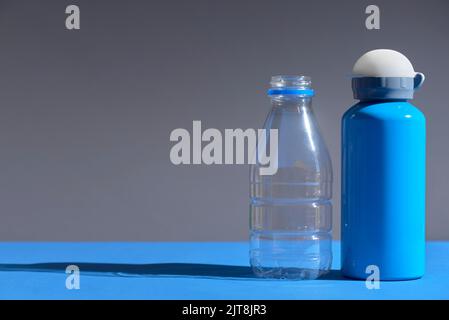 Pair of bottles, a plastic transparent disposable one and a blue metal reusable one. Concepts: sustainability, recycling, reusing, pollution, zero was Stock Photo