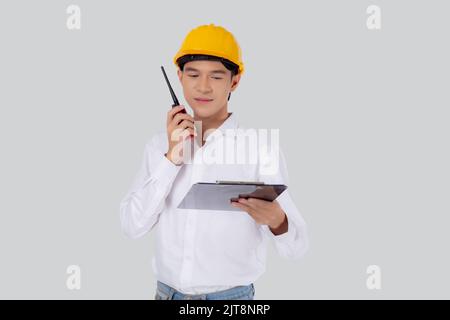 Portrait young asian man is engineer wearing helmet standing and using radio for speak with confident while holding report document isolated on white Stock Photo