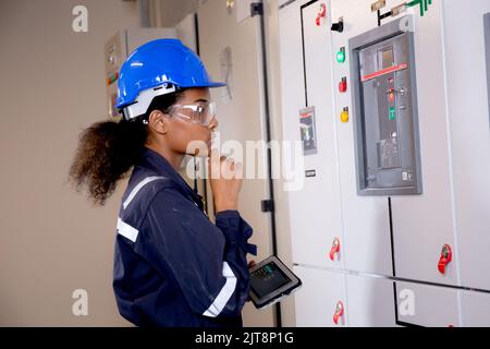 Electrical young asian woman engineer examining maintenance cabinet system electric and using tablet in control room at industrial factory, technician Stock Photo