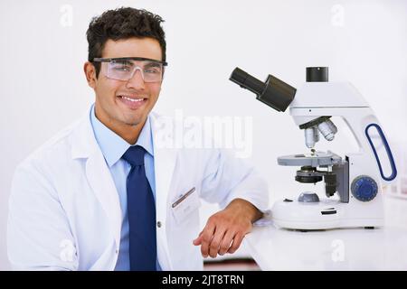 Hard at work in the lab. Portrait of a smiling lab technician using a microscope while sitting in a lab. Stock Photo