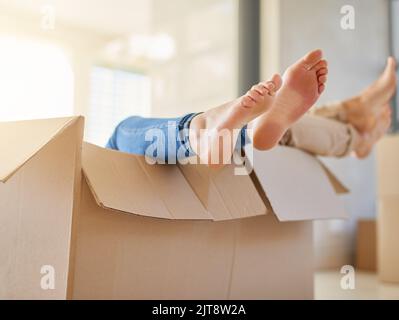 All packed up and ready to go. an unidentifiable young couple lying in a box together with their feet sticking out. Stock Photo