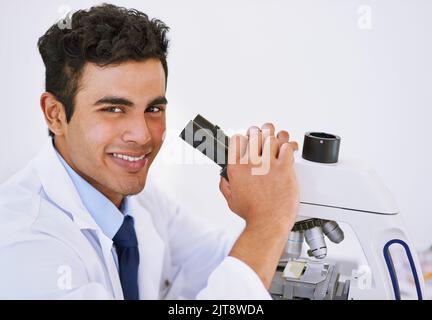 Getting results in the lab. Portrait of a smiling lab technician using a microscope while sitting in a lab. Stock Photo