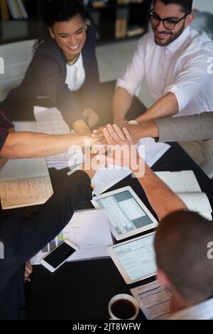 Succeeding is their top priority. a group of coworkers with their hands in a huddle while sitting together around a table in an office. Stock Photo