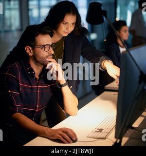 Bright ideas after dark. a businesswoman helping her colleague with his computer while they work overtime in the office. Stock Photo