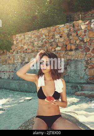 Shes one in a melon. a young woman enjoying a slice of watermelon on the beach. Stock Photo