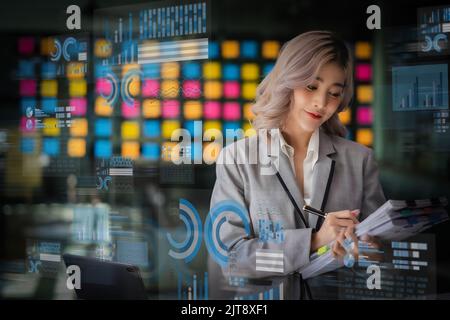 Young asian woman watching interface innovative Business technology on screens ai digital finance modern work infograph media Stock Photo