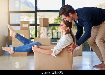 We dont take ourselves too seriously. a young man pushing his girlfriend around in a box while they move into their new home together. Stock Photo