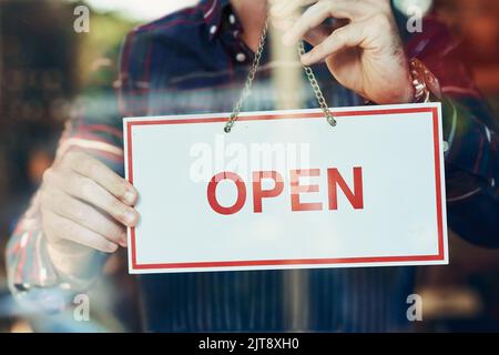 Opening day is here. Closeup shot of a young man hanging up an open sign in a shop window. Stock Photo