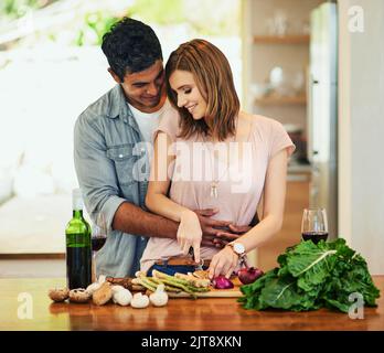 He couldnt help himself. a young man hugging his wife while she prepares dinner. Stock Photo